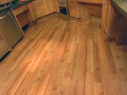 An image of a wooden floor, with planks of light brown wood arranged in a diagonal pattern. The wood grain is visible and adds texture to the surface. The floor is well-maintained and appears clean and shiny